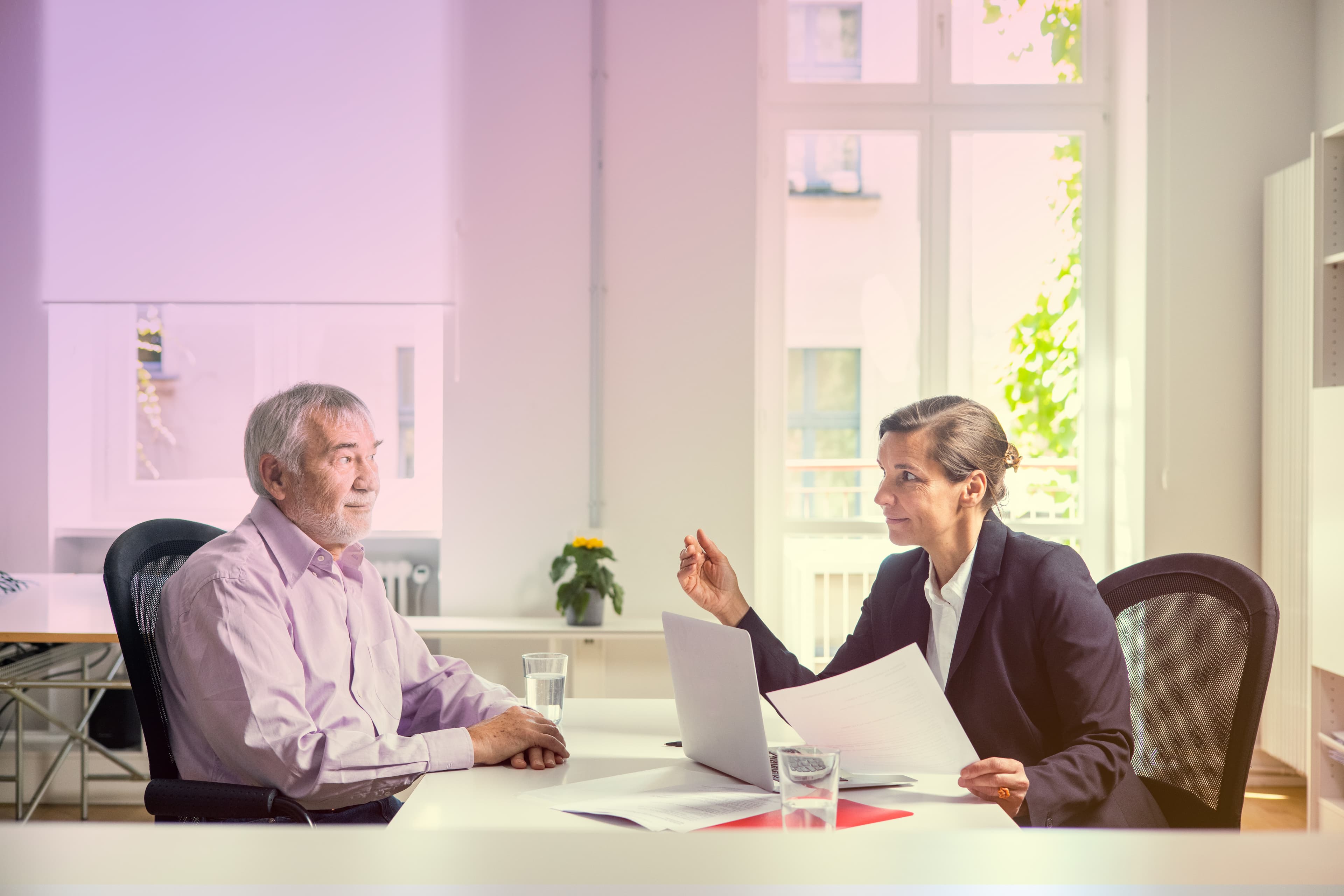 Eine Beraterin erklärt einem älteren Mann eine Akte.